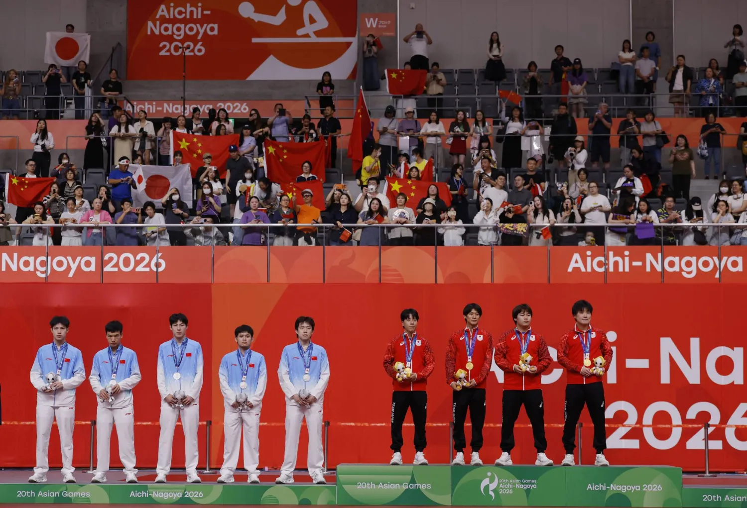 Asian Games - Aichi-Nagoya 2026 - Table Tennis - Men's Team Final - Sky Hall Toyota, Toyota, Japan - September 24, 2026   Gold medallists Japan's Tomokazu Harimoto, Sora Matsushima, Shunsuke Togami, Yukiya Uda and Hiroto Shinozuka celebrate on the podium after winning the Men's Team Final with silver medallists China's Youzheng Huang, Shidong Lin, Chuqin Wang, Ruibo Wen and Peng Xiang REUTERS/Andrew Couldridge