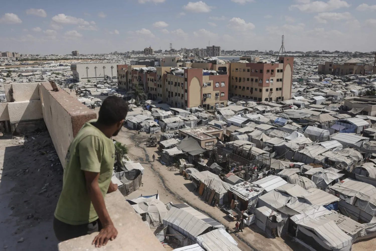 رجل يقف فوق مبنى ينظر إلى خيام فلسطينيين نازحين في منطقة المواصي بخان يونس في جنوب قطاع غزة (أ.ف.ب)
