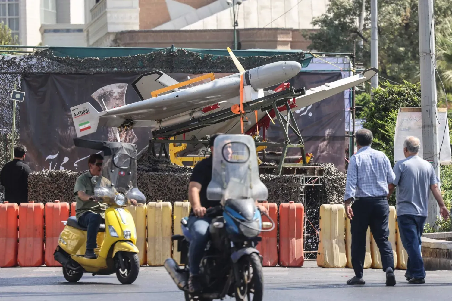 İranlılar, pazartesi günü Tahran'daki Baharistan Meydanı'nda sergilenen askeri İHA'ların önünden motosikletleriyle geçiyor (AFP)