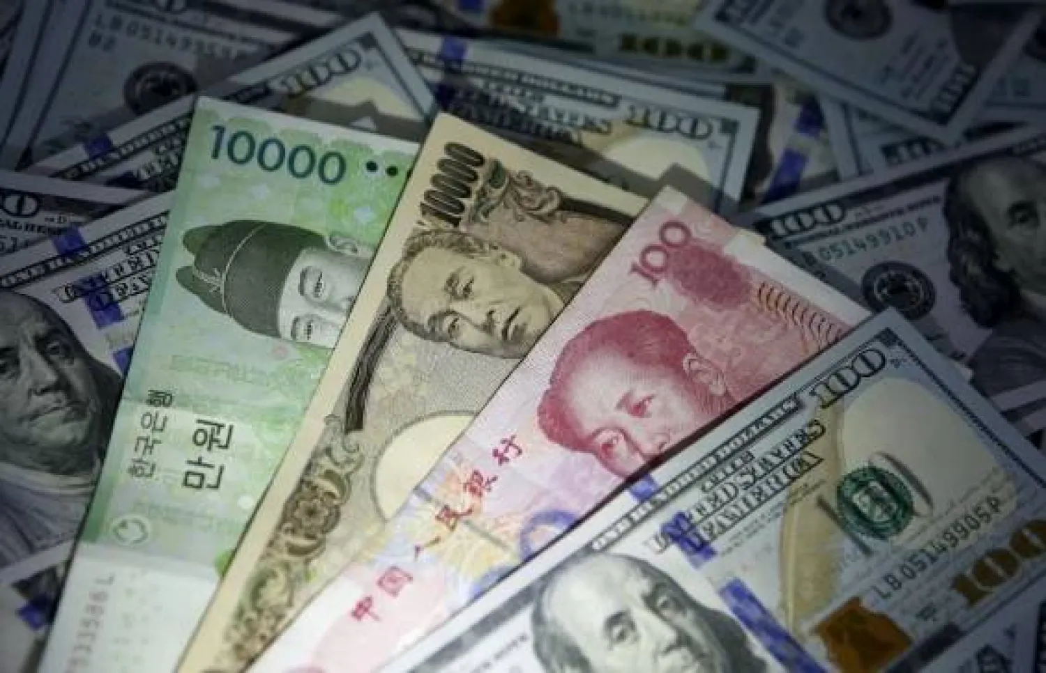 أوراق نقدية من الوون الكوري الجنوبي واليوان الصيني والين الياباني على أوراق نقدية من فئة 100 دولار أميركي (رويترز)