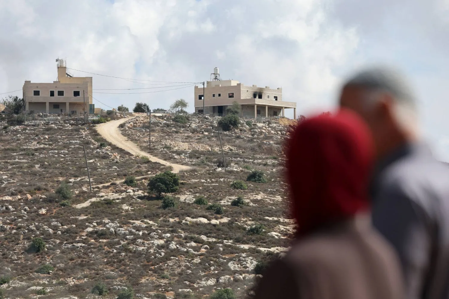 الفلسطيني محمود الطوباسي (60 عاماً) وزوجته عايدة (51 عاماً) يقفان بمنطقة تطل على منزلهما الذي تضرر جراء هجوم شنه مستوطنون إسرائيليون في جالود بالضفة الغربية المحتلة الثلاثاء (رويترز)