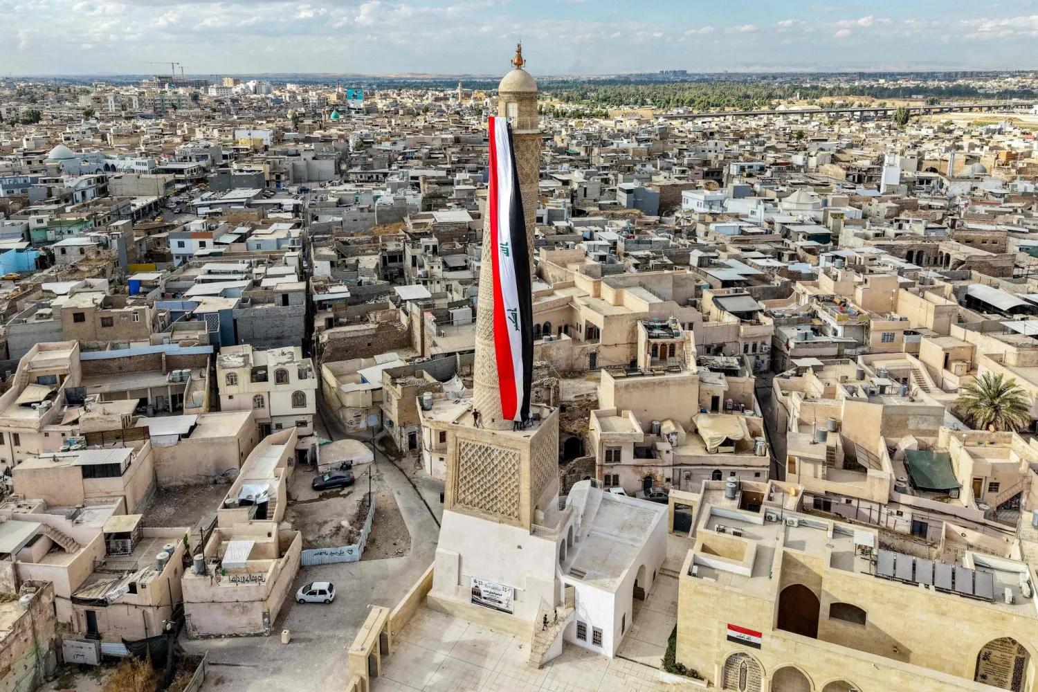 A giant Iraqi flag hangs off the reconstructed 12th century "Hadba" leaning minaret at the historic Great Mosque of al-Nuri in the old city of Mosul on September 29, 2026 as Iraq marks the withdrawal of the US-led anti-ISIS coalition forces from the country.  (Photo by Zaid AL-OBEIDI / AFP) 