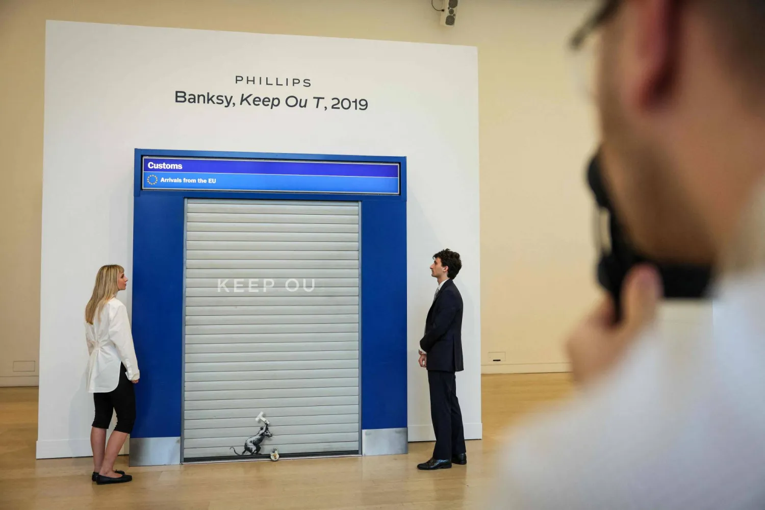 يقف مساعدون في المعرض بجوار عمل فني بعنوان «Keep Out» (ممنوع الدخول) لفنان الشارع البريطاني بانكسي أثناء الكشف عنه خلال معاينة صحافية لمزادات الفن الحديث والمعاصر ضمن فعاليات «أسبوع فريز» (Frieze Week) المرتقبة في دار «فيليبس» بوسط لندن (أ.ب)