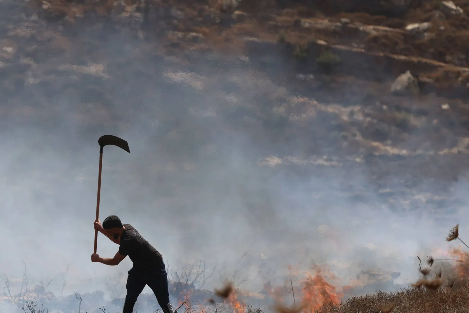 مزارع فلسطيني يحاول إخماد النيران في عصيرة القبلية جنوب نابلس بعد هجمات للجيش ومستوطنين (أ.ف.ب)