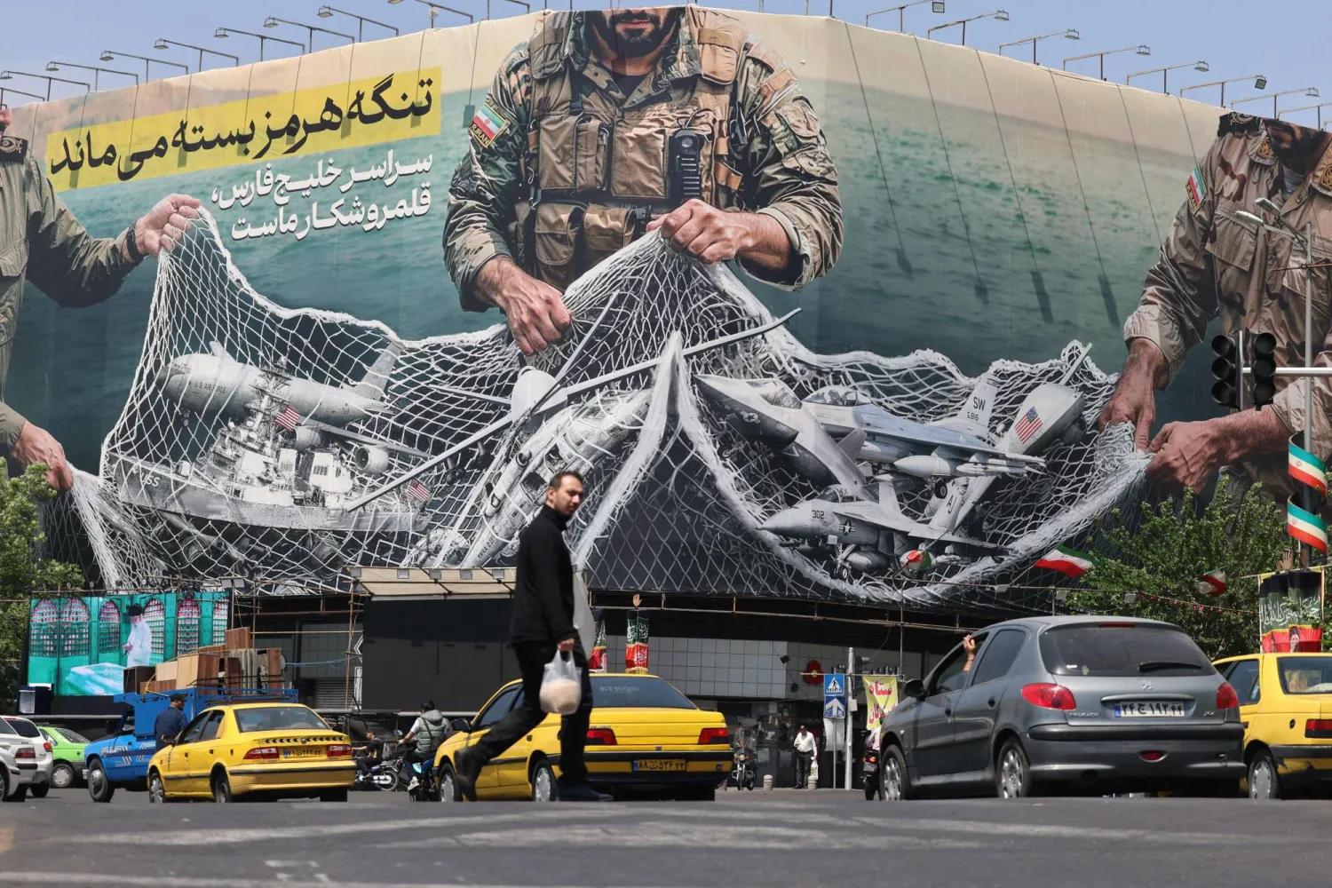 مركبات تمر بجوار لوحة إعلانية ضخمة تحمل عبارة «مضيق هرمز لا يزال مغلقاً» في ساحة الثورة بطهران (أ.ف.ب)