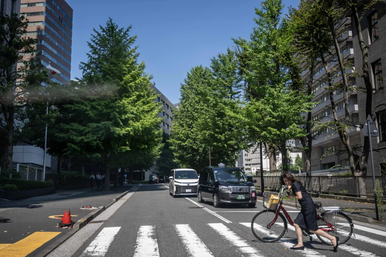 This picture taken on August 25, 2026 shows a woman crossing with her bike on a street in Tokyo. (Photo by Philip FONG / AFP)