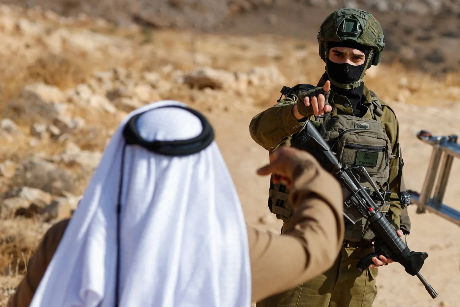 عنصر من القوات الإسرائيلية يشير بيده إلى فلسطيني أثناء قيامه بأعمال الحراسة خلال هدم مبنى فلسطيني بالقرب من الخليل في الضفة الغربية التي تحتلها إسرائيل (رويترز)