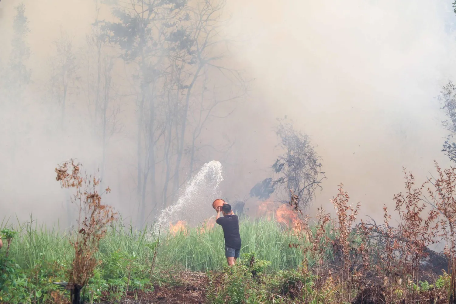 A man attempts to extinguish flames with a bucket amid thick smoke and fires burning through peatland in Palangkaraya, Central Kalimantan, on October 3, 2026. (Photo by REINA / AFP)