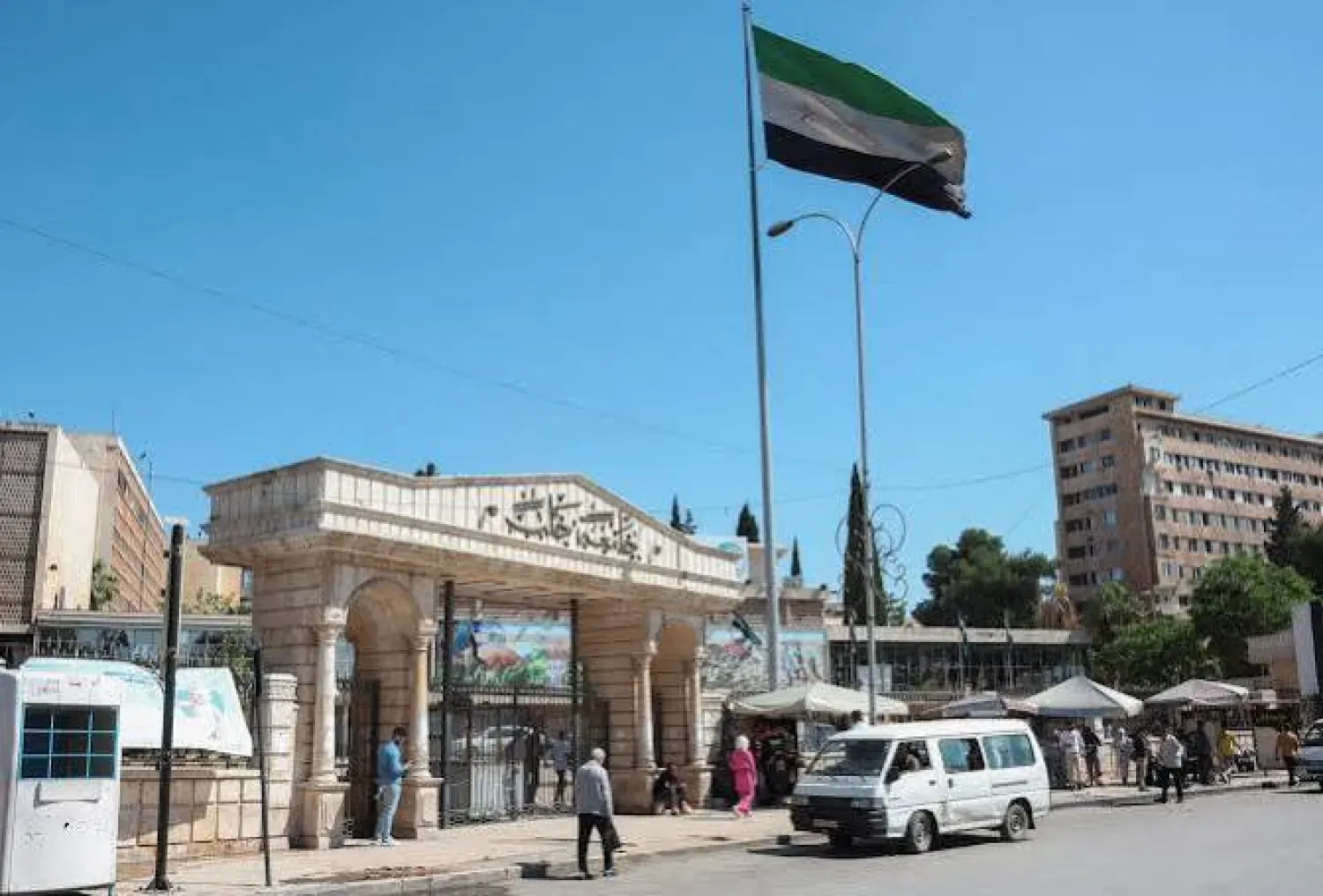 14 Mayıs 2025’te Halep Üniversitesi girişinin yakınından geçen bir kadın ve Suriye bayrağı (Reuters)