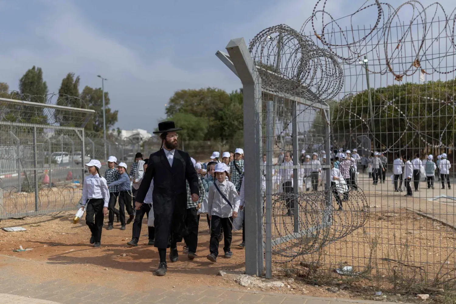 Breslov Yahudi cemaatinden bir kişi, 12 Ekim 2026’da İsrail’in orta kesimindeki Kfar Yona’da zorunlu askerlik hizmetine karşı düzenlenen protestoya katıldıktan sonra bir grup okul çocuğuna öncülük ediyor (AFP)