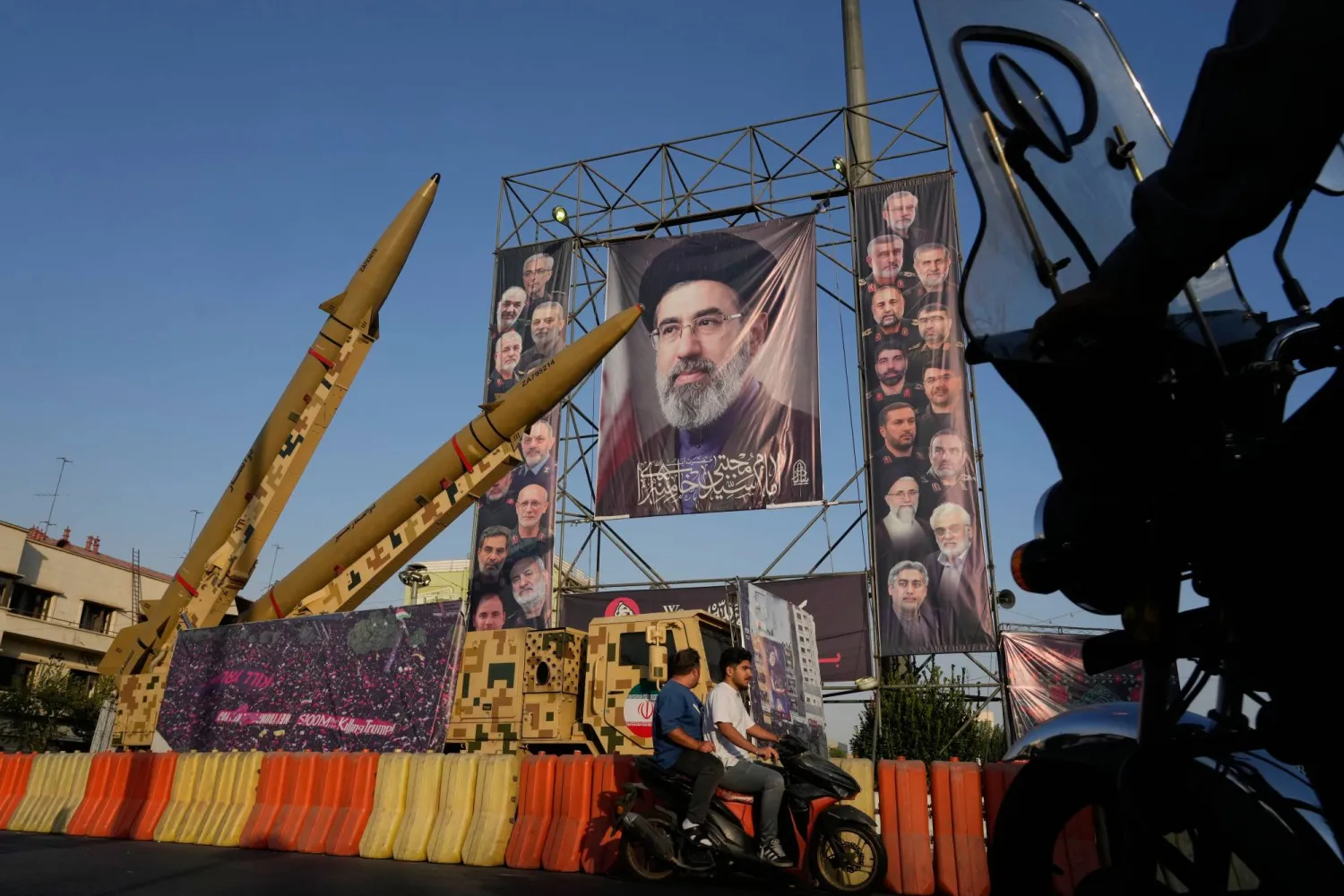 Motorbikes drive past Iranian missiles and banners showing portraits of the Iranian Supreme Leader, Mojtaba Khamenei, center, and the late armed forces commanders and nuclear scientists, who were killed in Israeli and US strikes, displayed in a military exhibition commemorating the anniversary of the start of the 1980-88 Iraq-Iran war at Baharestan Square, in Tehran, Monday, Sept. 28, 2026. (AP Photo/Vahid Salemi)