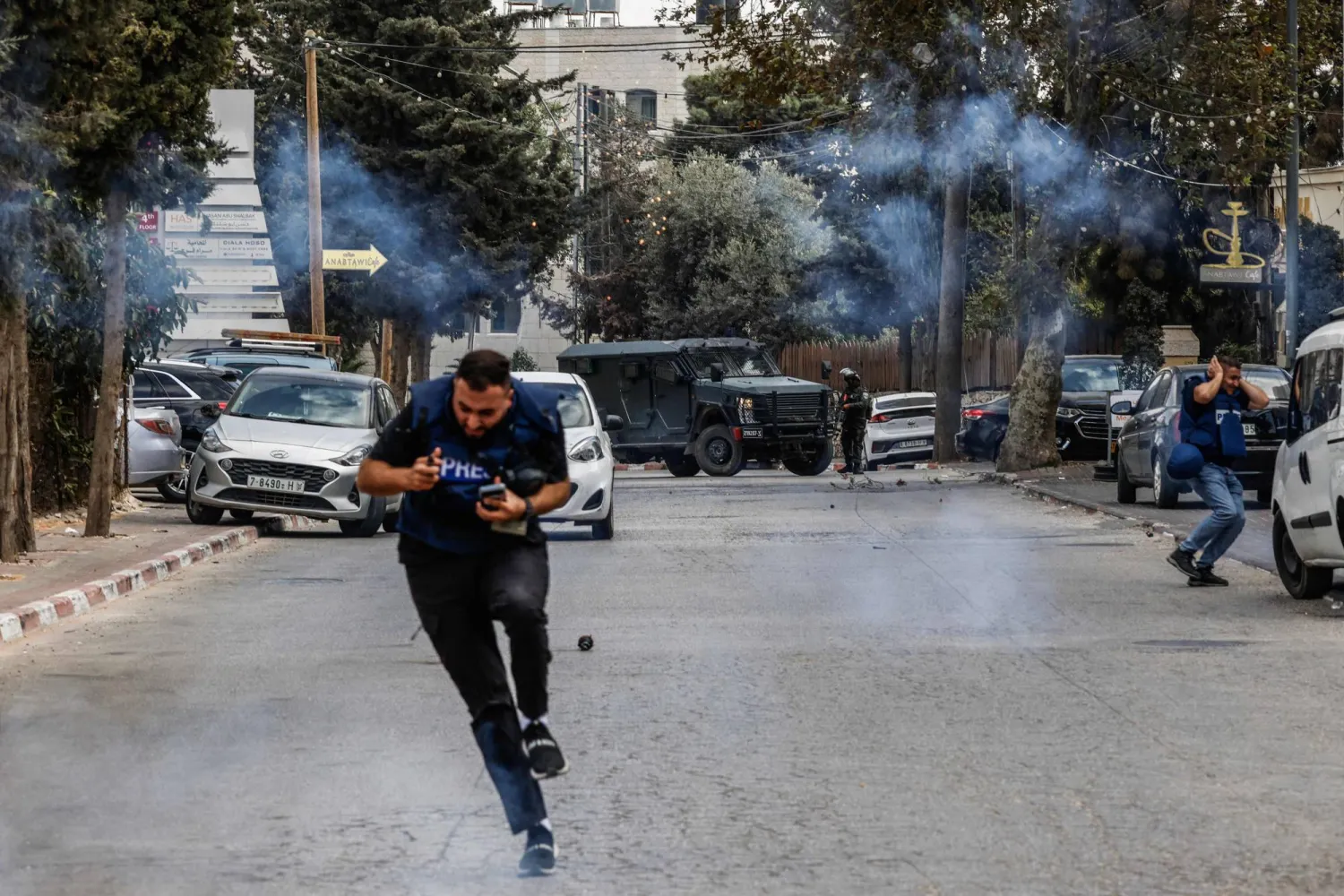 صحافيون يفرون من قنابل غاز أطلقتها قوات الجيش الإسرائيلي في أثناء مداهمة في رام الله بالضفة الغربية الثلاثاء (أ.ف.ب)
