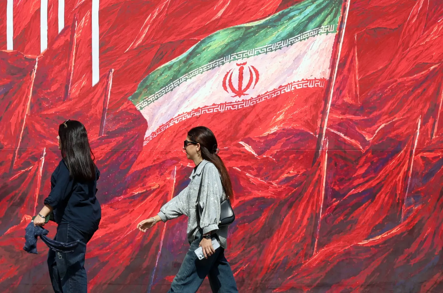 Iranian women walk past a banner featuring Iran’s national flag in a street in Tehran, Iran, 14 October 2026, amid the ongoing conflict between Iran and the United States. (EPA)