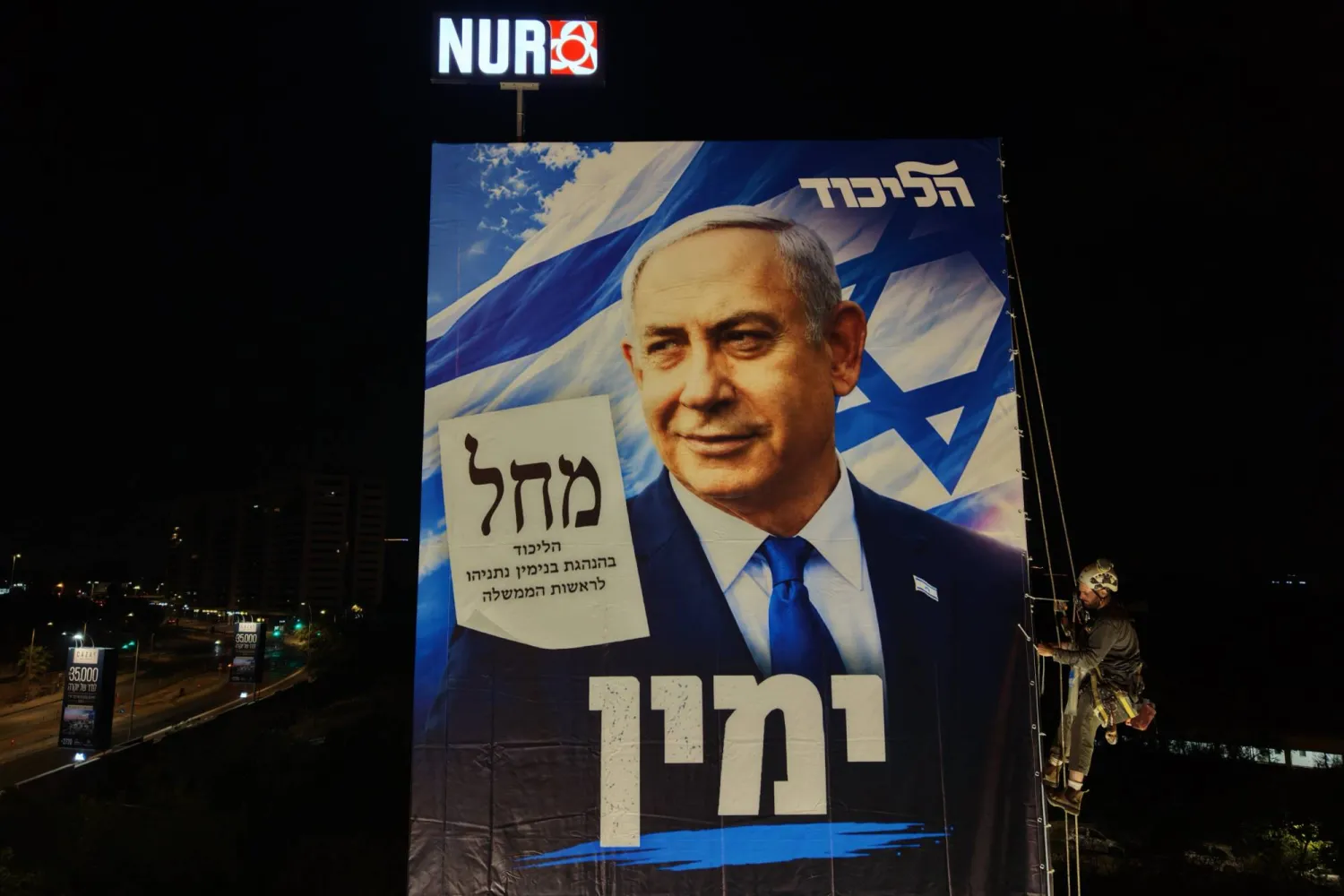 Rappelling workers install an election billboard featuring an image of Israeli Prime Minister Benjamin Netanyahu, and reading in Hebrew "It's either the Right or Palestine," in Ramat Gan near Tel Aviv, Israel, 18 October 2026. (EPA)
