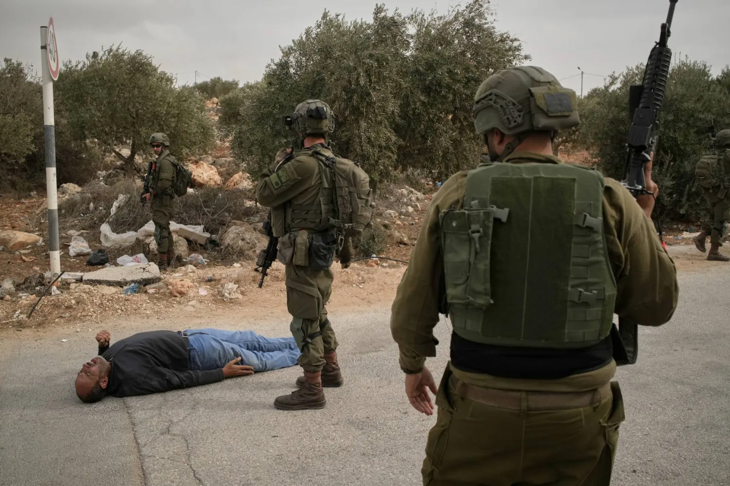 جنود إسرائيليون يقفون بجانب رجل فلسطيني جريح في أعقاب هجوم مستوطنين على فلسطينيين يقطفون الزيتون في الضفة الغربية (أ.ب)