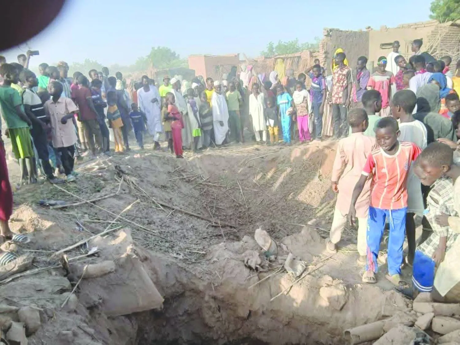 سودانيون يتفحصون فوهةً خلّفتها غارة بطائرة مسيّرة استهدفت في وقت سابق مخيماً للنازحين في وسط دارفور (الأمم المتحدة)