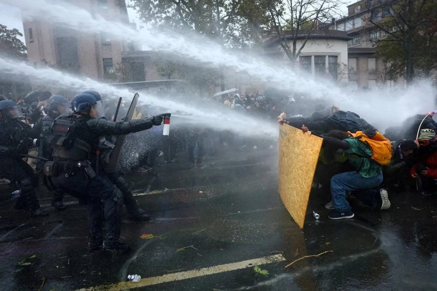 Protesters take cover behind a plywood board as French riot police and gendarmes use a water canon amid clashes during an authorized demonstration organized by labor unions in Paris as part of nationwide protests called by the "Yellow Vests" movement joined by French high school and university students against the cost of living and rising fuel prices, in France, October 24, 2026. (Reuters) 