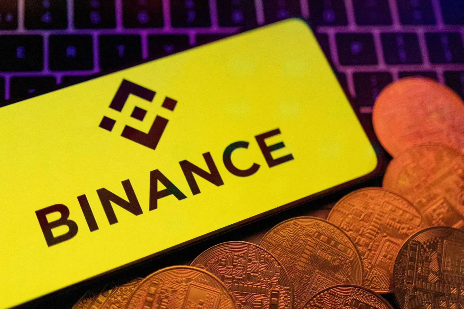 Binance logosu taşıyan bir akıllı telefon ve kripto para örnekleri (Reuters)