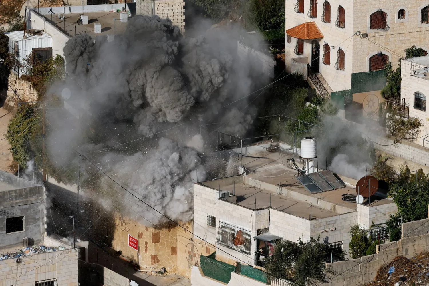 سحابة من الغبار تتصاعد بينما يهدم الجيش الإسرائيلي منزل فلسطيني في مدينة الخليل بالضفة الغربية (رويترز)