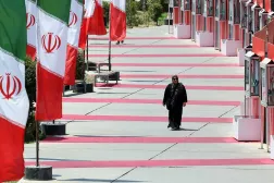 A woman walks next to Iranian national flags in a street in Tehran, Iran, 10 August 2025. (EPA)