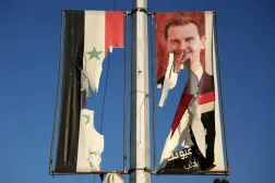 A billboard bearing a picture of Syria's ousted President Bashar al-Assad and a former national flag are torn by anti-government fighters in the northern city of Aleppo on Nov. 30. (AFP)
