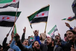 People celebrate and wave Syrian flags as they wait for a parade by the new Syrian army marking the first anniversary of the ousting of the Bashar al-Assad regime in Damascus, Syria, Monday, Dec. 8, 2025. (AP)
