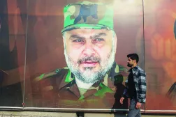 عراقي بأحد شوارع بغداد يمر أمام صورة لمقتدى الصدر مرتدياً الزي العسكري الخاص بـ«سرايا السلام»  (أ.ف.ب)