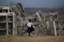 Filistinli bir çocuk, Gazze Şeridi'nin merkezindeki Nuseyrat mülteci kampında yıkılmış evlerin önünde duruyor (AFP)