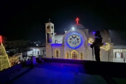 عنصر أمن سوري على سطح يطل على كنيسة القصير أثناء الاحتفال بإنارة «شجرة الميلاد» (متداولة)