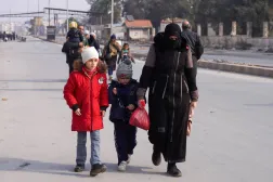 سورية تسير مع صغيريها في حلب بعد اتفاق دمشق وقوات ”قسد“ على خفض التصعيد مساء الاثنين (رويترز)
