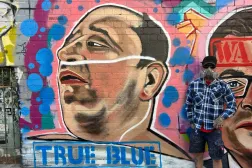 يقف فنان الشارع جارود جريش لالتقاط صورة بجانب لوحته التي تصور أحمد الأحمد وهو صاحب متجر سوري أسترالي يبلغ من العمر 43 عاماً والذي نزع سلاح أحد مهاجمي حادثة إطلاق النار في شاطئ بونداي بسيدني في ملبورن أستراليا (أ.ب) 