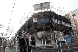 İranlı bir kadın, Tahran'da son dönemdeki hükümet karşıtı protestolar sırasında çıkan yangında hasar gören bir banka binasının önünden geçiyor (EPA)