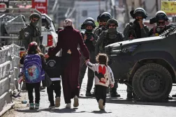 Filistinli bir kadın, çocuklarıyla birlikte, dün işgal altındaki Batı Şeria'da Ramallah yakınlarındaki Kafr Aqab mahallesine baskın düzenleyen İsrail işgal güçlerinin yanından geçiyor (AFP)