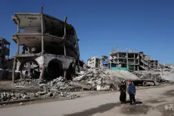 فلسطينيون يمرون أمام منازل بنايات مدمّرة بفعل الغارات الإسرائيلية في مدينة غزة أمس (رويترز)