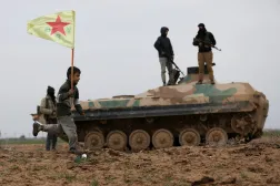 صبي يحمل علم «وحدات حماية الشعب الكردية» بجوار مركبة تابعة لـ«قسد» تنسحب من خطوط المواجهة على مشارف بلدة تل حمس 13 فبراير (رويترز)