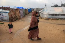 نازحة فلسطينية تسير حاملة طفلها على أرض بللتها مياه الأمطار بمخيم البريج للاجئين بوسط قطاع غزة يوم الثلاثاء (أ.ف.ب)