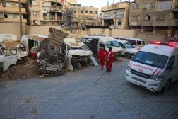 Filistinli sağlık çalışanları, Gazze Şeridi'nin güneyindeki Han Yunus'ta bulunan Filistin Kızılayı genel merkezinde tahrip olmuş ambulansların yanından geçiyor (AFP)