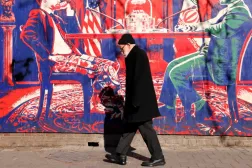 İran rejimi tarafından “casus yuvası” olarak adlandırılan Tahran'daki eski ABD büyükelçiliğinin dış duvarlarına çizilmiş bir duvar resminin önünden geçen bir adam, 1 Şubat 2026(AFP)