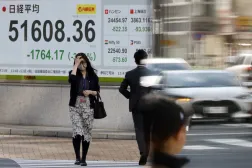 Tokyo Borsası’nın hisse senedi endeks panosunun önünden geçen insanlar (EPA)