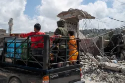 أطفال يقفون على متن شاحنة صغيرة أثناء مرورهم بجانب مبانٍ متضرّرة جرّاء غارة إسرائيلية في بلدة المنصوري جنوب لبنان (رويترز)