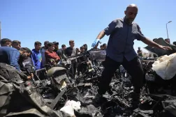 فلسطينيون في موقع استهداف سيارة بغارة جوية إسرائيلية في شارع صلاح الدين جنوب مخيم البريج وسط غزة الخميس (أ.ف.ب)