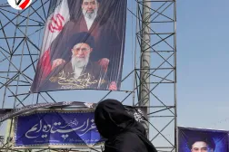 Tahran'da bir kadın, ABD-İsrail saldırılarında öldürülen baba Ali Hamaney ile oğlu Mücteba Hamaney’e ait afişlerin önünden geçiyor (AP)