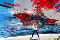 A woman walks past an anti-US and anti-Israel mural depicting missiles hitting an aircraft carrier in Tehran on May 26, 2026. (AFP)