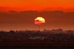 This picture taken from a position on the Israeli border with the Gaza Strip, shows the sun setting behind destroyed buildings in the besieged Palestinian territory on June 10, 2026. (Photo by Jack GUEZ / AFP)