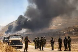 Israeli security forces stand guard along a road while behind smoke billows from an area reportedly set ablaze by Israeli settlers in the Palestinian village of Idna, west of Hebron in the occupied West Bank, on June 5, 2026. (AFP) 