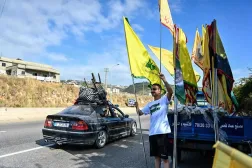 Displaced families drive past a man holding the Hezbollah party flag as they drive along the highway through the area of Jiyyeh as they return to their home villages in southern Lebanon on June 15, 2026. (AFP)
