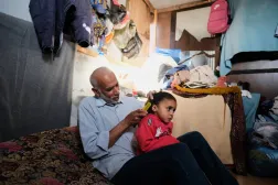 الفلسطيني محمود نوفل يمشط شعر حفيدته رنين (3 سنوات) والتي يتولى رعايتها بعد مقتل والديها في غارة إسرائيلية على خان يونس (أ.ب)