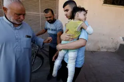 فلسطيني يحمل طفلاً أصيب بغارة إسرائيلية قتلت والديه في مستشفى «شهداء الأقصى» بدير البلح وسط قطاع غزة الأربعاء (رويترز)