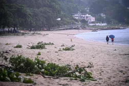 People walk on a beach with debris from Typhoon Noul which passed close to Hong Kong on July 26, 2026. (Photo by Peter PARKS / AFP)