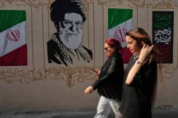 إيرانيتان تمران قرب صورة للمرشد الإيراني السابق علي خامنئي الذي قُتل في الضربات الأميركية - الإسرائيلية في 28 فبراير وأعلام إيرانية وسط طهران - 20 أغسطس 2026 (أ.ب)